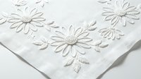 White linen fabric with delicate embroidered daisy flowers and leaves in raised threadwork, perfect for home decor, table linens, and craft projects.