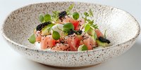 Fresh salmon sashimi cubes with black caviar, microgreens and herbs in speckled ceramic bowl on white background. Gourmet seafood dish for fine dining menu.