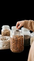 Glass jars filled with almonds, nuts, and grains, with a hand opening a lid, isolated on transparent background, ready for food, kitchen, and healthy lifestyle design use.