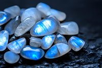 Natural moonstone gems with bright blue adularescence on dark background, showing iridescent play of light and mystical glow characteristic of precious stones.