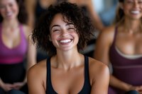 Happy mixed-race woman laughing during group fitness class with diverse female friends in background wearing colorful athletic wear at gym studio.
