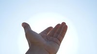 Close-up of an open palm facing upward against a light sky background, showing skin texture and natural hand position for concepts of giving, receiving, or offering support.