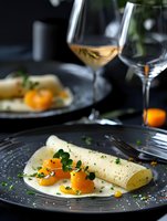 Elegant crepe with cured salmon spheres and microgreens served on dark plate with white wine. Fine dining restaurant atmosphere with moody lighting.
