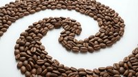 Roasted coffee beans arranged in a spiral swirl pattern on white background, isolated for design use on merchandise and packaging materials.