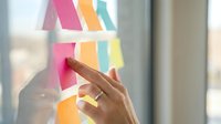 Business professional organizing colorful sticky notes on glass window for project planning and workflow management in modern office environment.