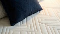 Dark navy pillow resting on quilted cream mattress with geometric stitching pattern, ideal for bedding, home decor, and interior design projects.