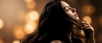 Young woman with flowing dark hair in motion against warm golden bokeh lights background creating dreamy atmosphere for beauty and wellness concepts.