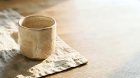 Rustic ceramic cup with weathered finish sitting on crumpled linen fabric in natural sunlight, perfect for home decor and lifestyle content.