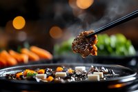 Steaming hot Asian cuisine with chopsticks holding glazed meat over dark plate with vegetables and bokeh lights in background, food photography for restaurant menus.