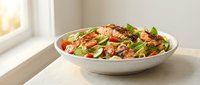Fresh Mediterranean pasta salad with cherry tomatoes, basil leaves and mixed greens in white bowl on kitchen counter for healthy meal preparation.