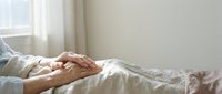 Caring hands of elderly couple holding together in bed showing love, support and companionship in comfortable bedroom setting with soft natural lighting.