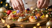 Hands preparing festive holiday appetizers with salmon, cream cheese and garnishes on wooden board with Christmas decorations and warm lights.