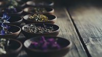 Aromatic dried herbs and flowers in wooden bowls on rustic table, moody natural lighting creates atmospheric composition for wellness and herbal tea concept.