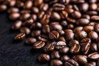 Fresh roasted coffee beans scattered on dark slate stone background, macro shot with selective focus showing rich brown color and natural texture.