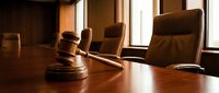Wooden gavel on polished conference table in modern courtroom with leather chairs and natural window lighting for legal proceedings and justice concepts.