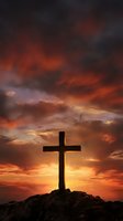 Wooden cross silhouette against dramatic sunset sky with orange and red clouds on rocky hill for Easter and Christian faith concepts.
