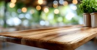 Empty wooden table with natural wood grain pattern against blurred bokeh background with decorative plant, suitable for product display or food photography.