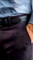 Close-up of businessman wearing formal attire with leather belt and hand in pocket of purple trousers, paired with light blue dress shirt for professional look.