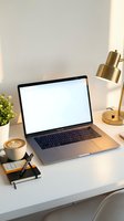 Modern home office workspace with open laptop displaying blank screen, coffee cup with latte art, brass desk lamp and small plant on white desk for remote work.