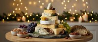 Festive cheese tower stacked in a Christmas tree shape, surrounded by grapes, figs, nuts, and bread on a wooden board with warm bokeh lights.