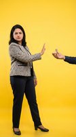 Professional South Asian businesswoman in suit rejecting offer with stop gesture on bright yellow background for corporate communication concepts.