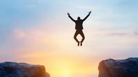 Silhouette of person jumping between mountain cliffs at sunset, expressing freedom, achievement and success against dramatic sky background.