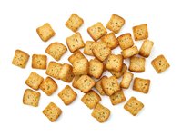 Crispy square crackers with sesame seeds and herbs scattered on white background, isolated for food packaging, menus, and culinary design projects.