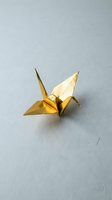 Golden origami crane folded from metallic paper on neutral gray background symbolizing peace, hope and traditional Japanese art for meditation concepts.