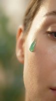 Young woman applying green jade gua sha facial massage tool for skincare routine and natural beauty treatment in soft morning light.
