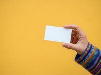 Hand holding blank white card against bright yellow background, suitable for business card mockups, promotional designs, and marketing materials.