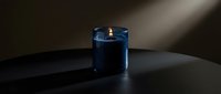 Blue scented candle burning with warm flame on dark surface creating cozy atmospheric lighting for relaxation and home decor ambiance.