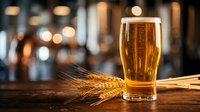 Golden beer glass with wheat stalks on wooden bar counter in warm pub atmosphere with bokeh lights creating cozy drinking establishment ambiance.