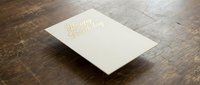 Elegant white business card with gold foil lettering on rustic wooden surface for corporate branding and professional identity design.