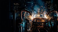 Industrial robotic welding arms creating bright sparks in automated manufacturing facility with dramatic lighting and metal fabrication equipment.