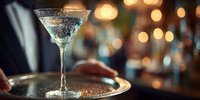 Elegant martini cocktail with sugar rim on silver tray, served against warm bokeh lights in upscale bar atmosphere.