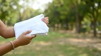 Hands holding blank white envelope outdoors in park setting with green trees, suitable for mail, correspondence, and communication concepts.