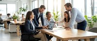 Diverse business team collaborating in modern office meeting room with laptops and documents during productive brainstorming session.