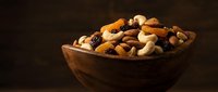 Mixed nuts and dried fruits in wooden bowl on dark background for healthy snacking and cooking ingredients.