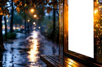 Cozy evening cityscape with glowing street lights reflecting on wet pavement, viewed through window with autumn leaves and raindrops, creating atmospheric bokeh effect.