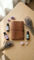 Wellness flat lay with leather journal, essential oil bottles, dried lavender, amethyst and rose quartz crystals on wooden table for aromatherapy and mindfulness.