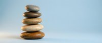 Balanced stack of smooth river stones creating zen meditation tower against soft blue sky background for wellness and mindfulness concepts.