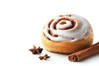 Fresh baked cinnamon roll with white cream cheese frosting, served with aromatic star anise and cinnamon sticks on white background, isolated food photography.