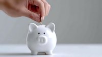 Hand inserting coin into white ceramic piggy bank for savings and financial planning concept on clean background.