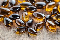 Golden vitamin E capsules scattered on rustic wooden surface for health and wellness supplement photography and medical content.