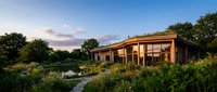 Modern eco-friendly house with large windows surrounded by lush garden landscape at sunset. Sustainable architecture design for residential living concepts.