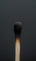 Burnt wooden matchstick with charred black head on dark gray background symbolizing burnout, exhaustion, failure, or end of resources concept.