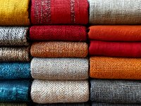 Colorful fabric rolls stacked in rows showing various textures and materials for textile industry, fashion design, upholstery and interior decoration projects.