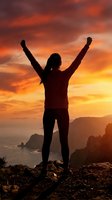 Silhouette of victorious woman with raised arms celebrating success at dramatic sunset over ocean cliffs. Achievement and triumph concept for motivation content.