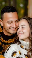 Young diverse couple in matching knit sweaters share intimate moment outdoors with gentle smiles and closed eyes, expressing romance and tenderness.