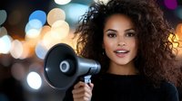 Young African American woman with curly hair holding megaphone against blurred city lights background, expressing leadership and communication concept. Activism and speaking out.
